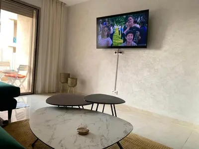 a living room with two tables and a tv on the wall at La Perla de Marrakech Appart de Luxe in Marrakech