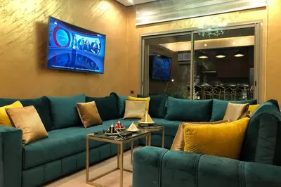 a living room with a blue couch and a tv at Cosy Loft Emeraude Marrakech Prestigia Golf City in Marrakech