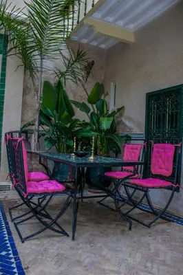 a glass table with pink chairs and plants on a patio at Riad Dar Habiba by Garden Wonders in Marrakech