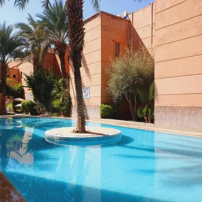 a swimming pool with a palm tree in front of a building at Chez Jasmeene in Marrakech