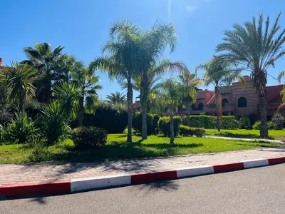 a road with palm trees and a house in the background at Duplex Atlas Golf Resort Pοοl νieω Seriniτყ & Cαlm in Marrakech