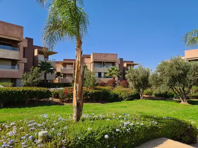 a palm tree in a park in front of a building at Appartement chic avec jardin a Prestigia Golf City in Marrakech