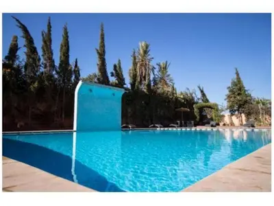 a large blue swimming pool with trees in the background at Appartement aux portes de la palmeraie in Marrakech