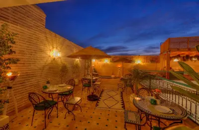 a patio with tables and chairs on a balcony at night at riad paradis blanc in Marrakech