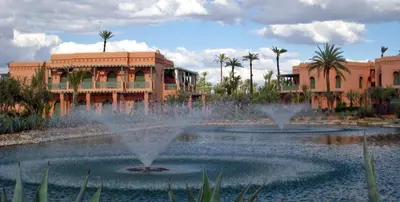a fountain in front of a building with palm trees at Palmeraie Village in Marrakech