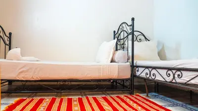 two twin beds in a room with a rug at Hotel imouzzer in Marrakech