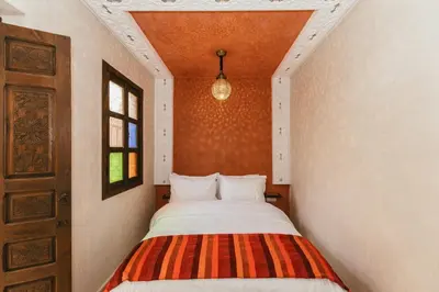 a small bedroom with a bed with a striped blanket at L'Emeraude de la Médina in Marrakech