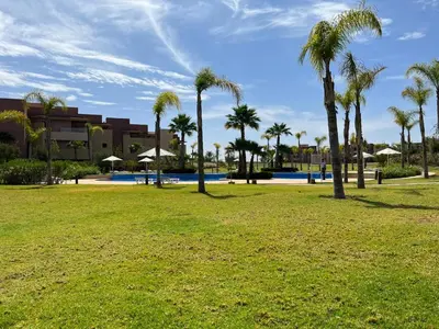 a park with palm trees in front of a building at Appartement de Luxe -Prestigia Marrakech Golf City in Marrakech