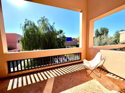 a balcony with a white chair and two large windows at Al Maaden Ryad 69 a Marrakesh in Marrakech