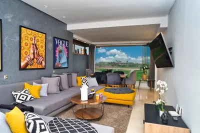 a living room with a gray couch and yellow accents at Prestigia, superbe appartement, vue sur golf, piscine et Atlas in Marrakech