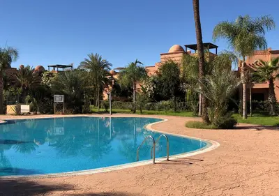 a swimming pool in front of a resort with palm trees at Atlas Views By Golf Resort in Marrakech