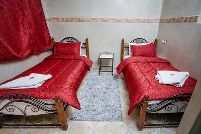 two beds in a room with red comforter at Hôtel Faouzi in Marrakech