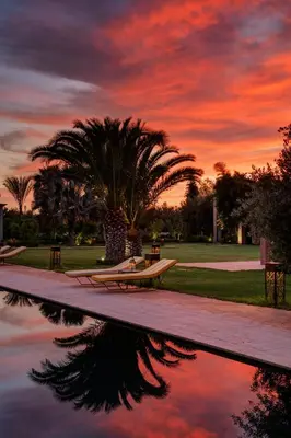 a sunset over a pool with a bench and palm trees at Pavillon Terra Ababila en Exclusivité in Marrakech
