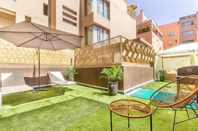 an apartment patio with chairs and an umbrella and grass at NEW!, Jardin privé, transats, barbecue in Marrakech