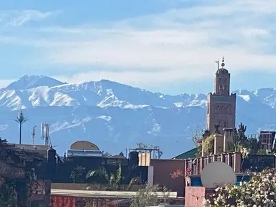a building with a clock tower with mountains in the background at Riad Al Massarah in Marrakech