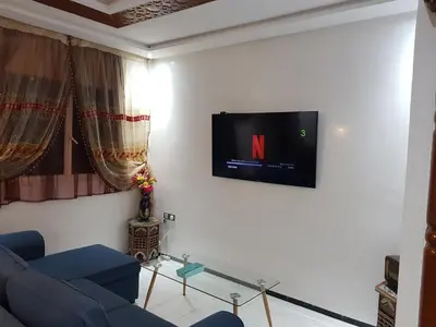 a living room with a blue couch and a tv on a wall at Appartement warda in Marrakech