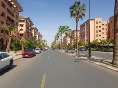 an empty street with palm trees and cars parked on it at Appartement warda in Marrakech