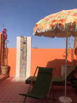a chair and an umbrella next to a wall at Riad Imndi in Marrakech
