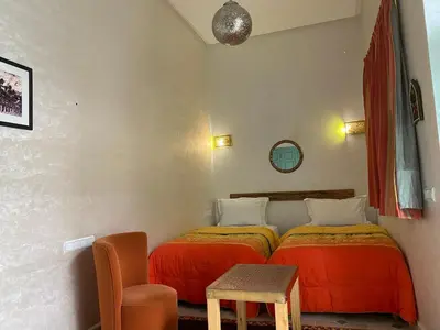 a bedroom with two beds and a table and a chair at Riad Deux Palmiers in Marrakech