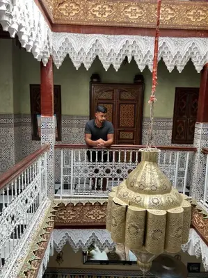 a man sitting on a balcony with a chandelier at Riad Elijah Marrakech & SPA in Marrakech