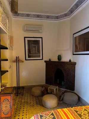 a living room with a fireplace with two ottomans and a bed at Riad Hugo in Marrakech