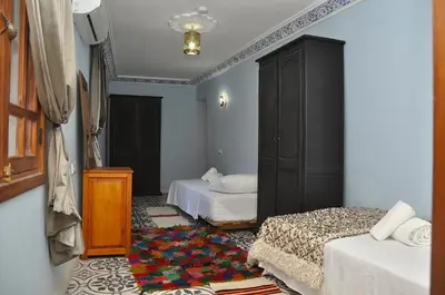 a bedroom with two beds and a cabinet and a rug at Dar Aouinti in Marrakech