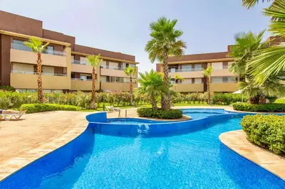 a swimming pool in front of a building with palm trees at Appartement de luxe prestigia Golf Resort in Marrakech