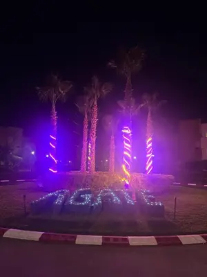 a lit up fountain with palm trees at night at Appartement de luxe prestigia Golf Resort in Marrakech
