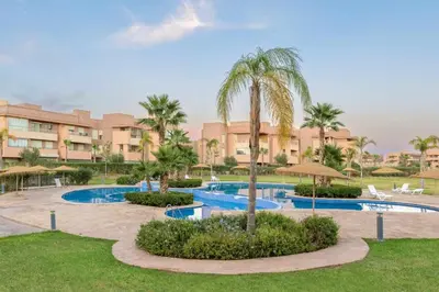 a resort with two pools and palm trees and buildings at Prestigia golf city porte agate in Marrakech