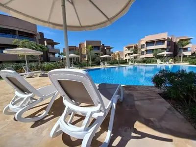 two white chairs and an umbrella next to a swimming pool at Prestigia golf city porte agate in Marrakech