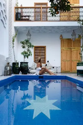 a woman sitting on a couch next to a swimming pool at Riad Botanica in Marrakech