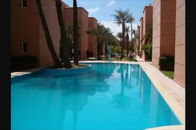 a blue swimming pool next to a building with palm trees at Jolie petit Riyad avec piscine belle terrasse wifi in Marrakech