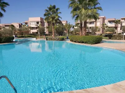 a large blue swimming pool with palm trees and buildings at Appartement de luxe Prestigia Opale in Marrakech