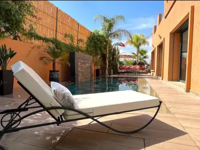 a white chair sitting next to a swimming pool at Belle et spacieuse villa au Golf Amelkis Marrakech in Marrakech