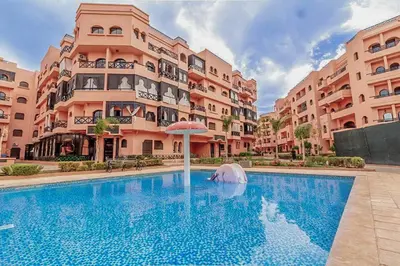 a swimming pool with an umbrella in front of a building at Les Jardins Sakar - Marrakech - Deux Chambres Exceptionnelle in Marrakech