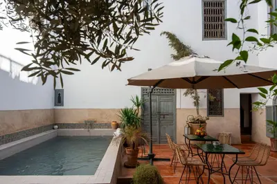 a pool with tables and chairs and an umbrella at Riad le Jardin de Mina in Marrakech