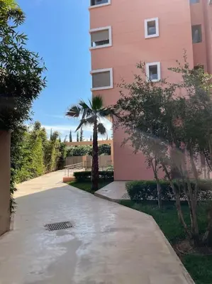 a pink building with a palm tree next to a sidewalk at Duplex Cosy dans résidence avec piscine in Marrakech