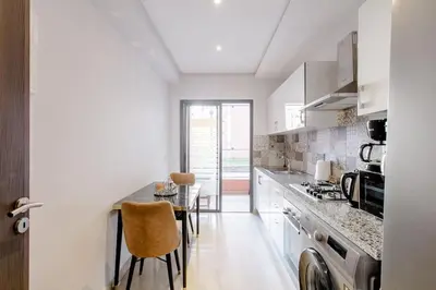 a kitchen with white cabinets and a table with chairs at Appartement résidence Marrakech haut standing piscine in Marrakech