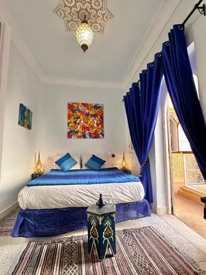 a bedroom with a bed with blue curtains and a window at Riad Shaden in Marrakech