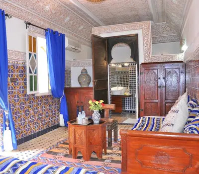a bedroom with a bed and a table and blue curtains at Riad Shaden in Marrakech