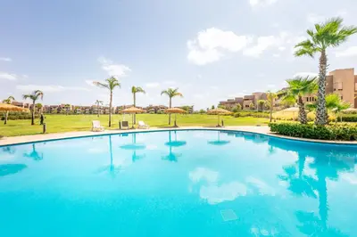 a large blue swimming pool with palm trees in the background at Perle Rare a Prestigia - Vue Sur Golf in Marrakech
