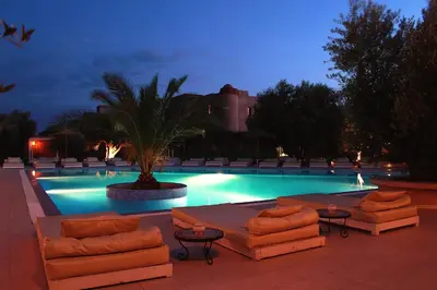 a swimming pool at night with couches and a palm tree at La Maison Des Oliviers in Marrakech