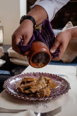 a person pouring sauce into a pot next to a plate of food at Kenzi Menara Palace & Resort in Marrakech