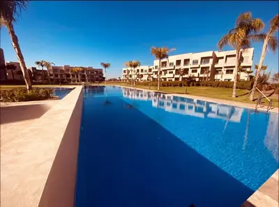 a large blue swimming pool with palm trees and buildings at Ehden Properties - Appt luxueux dans la residence golfique Prestigia Argan in Marrakech