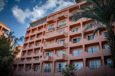 a pink hotel with a palm tree in front of it at Imperial Holiday Hôtel & spa in Marrakech