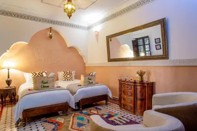 a bedroom with two beds and a mirror and chairs at Riad Itrane in Marrakech