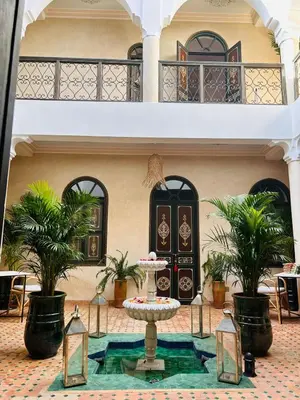 a courtyard with a table and palm trees in front of a building at Riad Bamaga in Marrakech