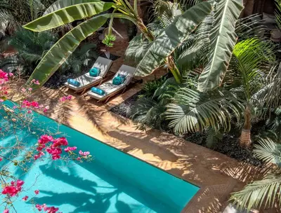 a swimming pool with two lounge chairs and palm trees at La Sultana Marrakech in Marrakech