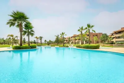 a large blue swimming pool with palm trees and buildings at Résidence Golfique PJ, jardin, piscine in Marrakech