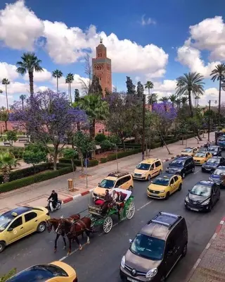 a busy city street with cars and a horse drawn carriage at Super appartement familial avec piscine à Prestigia Marrakech in Marrakech
